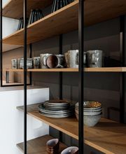 Moderne, hochwertige Designküche mit weißer Kücheninsel, dunklen Glasfronten und offenem Regal aus massivem Holz. Handgefertigtes Keramikgeschirr in natürlichen Grau- und Brauntönen setzt warme Akzente und unterstreicht den minimalistischen, modernen Wohnstil.