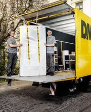 Zwei Mitarbeiter verladen ein verpacktes Möbelstück in einen DMS LKW