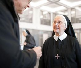 Ältere Ordensschwester im schwarzen Habit mit weißem Schleier während eines persönlichen Gesprächs mit einem Mann.