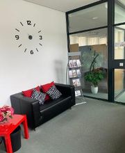 Aufenthaltsraum mit einem schwarzen Ledersofa, roten Kissen und einem roten Beistelltisch. Darüber hängt eine stilvolle, große Uhr an der Wand.