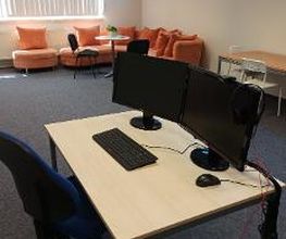 PC-Arbeitsplatz mit zwei Bildschirmen, Tastatur und Maus. Im Hintergrund ist die Sitzecke zu sehen.
