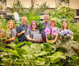 Blumen-Risse Team aus der Abteilung Floristik, Blumenmarkt Lüdinghausen, Baumschule, Keramik, Zimmerpflanzen und Beetware steht zwischen grünen Zimmerpflanzen im Blumenmarkt Lüdinghausen.