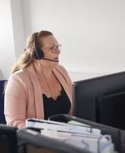 Teilnehmerin sitzt am Arbeitsplatz und kommuniziert mit den anderen Teilnehmenden und Dozent:innen über Headset.