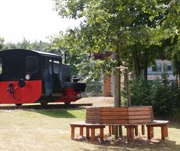 Außenbereich Pausenbereich mit Holzbank und Lokomotive.