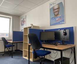 Zwei PC-Arbeitsplätze mit 2 Bildschirmen, einem Bürostuhl, Tastatur, Maus und Headset. Darüber hängen WBS TRAINING Plakate.