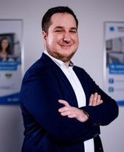 Portrait von einem männlichem Mitarbeiter im Anzug, der freundlich in die Kamera lächelt.