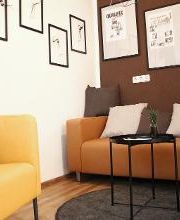 Gemütliche Sitzecke bestehend aus einem orangenen Ledersofa mit Kissen und einem gelben Sessel sowie einem kleinen Beistelltisch. An der Wand hängen stilvolle Bilder.