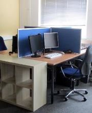 Heller Schulungsraum mit zwei PC-Arbeitsplätzen und einem Regal.