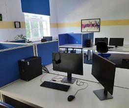 Arbeitsbereich mit 2 Computer-Bildschirmen, einer Tastatur, Maus und blauen Trennwänden. An der Wand im Hintergrund hängt ein buntes Bild.