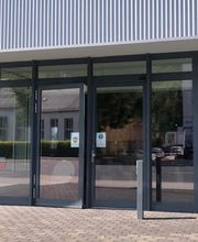 Außenansicht des Eingangsbereichs mit Glastür und großen Fenstern.