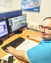 Teilnehmer schaut strahlend in die Kamera und arbeitet am PC und freut sich das sein Kurs gut läuft