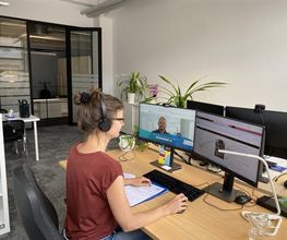 Eine Kollegin der Region Leipzig am PC-Arbeitsplatz mit 2 Bildschirmen und Headset.