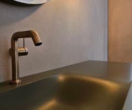 Luxus-Armatur Detail: Hochwertige, gold-bronzene Armatur an einem dunklen Waschtisch vor einer fugenlos gestalteten Wandfläche – edles Küchendesign oder Bad-Detail.