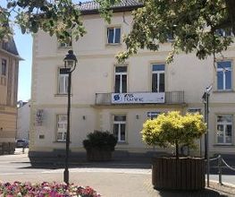Gelbes Gebäude mit Balkon an dem ein WBS TRAINING Banner hängt. Davor eine Straße und mehrere Pflanzen.