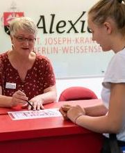 Empfang im Krankenhaus, Mitarbeiterin erklärt Patientin den Weg anhand des Lageplans