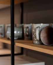Detailaufnahme eines modernen, offenen Küchenregals aus hochwertigem Holz mit handgefertigten Keramiktassen in natürlichen Grau- und Brauntönen. Die Kombination aus dunklem Metallrahmen, warmem Holz und minimalistischer Keramik unterstreicht das elegante, zeitgemäße Küchendesign.