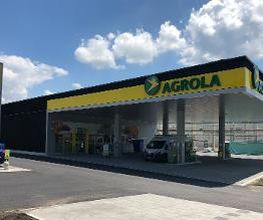 AGROLA Tankstelle in Konolfingen; überdacht mit TopShop; Vorplatz im Vordergrund, links Totem-Schild mit AGROLA Logo, digitaler Preisanzeige von Treibstoff, AdBlue, TopShop und selfwash logo