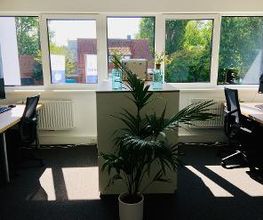 Zwei Schreibtische im Trainingsraum mit jeweils zwei Bildschirmen. Tastatur, Maus und Headset. Eine große Fensterfront mit Blumen.