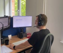 Ein Teilnehmer sitzt an seinem Arbeitsplatz vor 2 PC-Bildschirm und trägt sein Headset.