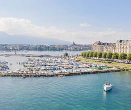 Panoramic view of Geneva’s waterfront with The Woodward hotel overlooking Lake Geneva and the Jet d’Eau fountain.