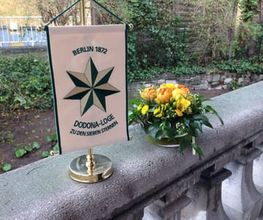 Ein kleiner Wimpel der Dodona Loge Berlin neben einem Blumengesteck.