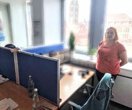 Teilnehmerin steht am Arbeitsplatz am Fenster