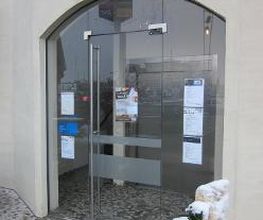 Außenansicht des Gebäudes mit gläserne Haupteingangstür und weißer Hauswand.