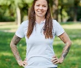 Vanessa Tonn steht im weißen T-Shirt mit WBS GRUPPE Logo in der grünen Natur und lächelt freundlich.