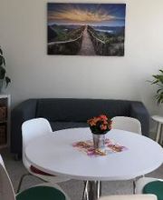 Aufenthaltsraum mit Sofa und Beistelltisch, auf dem Pflanzen stehen. Davor ein Tisch mit 5 Stühlen.