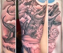 Realistisches Black-and-Grey-Tattoo einer Abenteurerin, die auf einem Alligator reitet, mit Peitsche, Wolken und dynamischer Action-Szene.