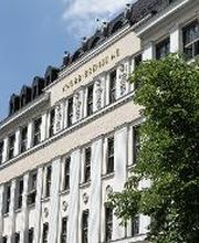 Front of the historic Knorr-Bremse Group building at the company's headquarters in Munich, with the words Knorr-Bremse AG in gold letters at the top. To the right of the building is a large chestnut tree with green leaves.
