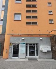 Außenansicht vom Gebäude der Einrichtung mit einer orangenen Fassade und mehreren Schildern sowie Briefkästen im Eingangsbereich.