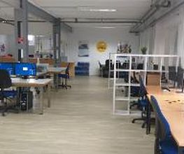 Schulungsraum mit mehreren Arbeitsbereichen, die jeweils mit 2 PC-Bildschirmen, Tastatur, Maus und Headset ausgestattet sind. Weiße Regale dienen als Abtrennung.