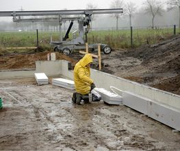 Mitarbeiter von AS-Bau arbeitet bei Regen an der Fundamentwand eines Neubaus.