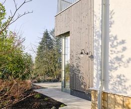 Architektonisches Detail an der Schnittstelle zwischen Bestand und Anbau: Die Kombination aus Putz, Naturstein, Holzverschalung und Metall schafft ein harmonisches Gesamtbild mit handwerklicher Präzision.