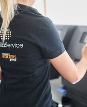 mediaService Bremen | Full-Stack Werbeagentur - Eine Mitarbeiterin in dunkler Arbeitskleidung bedient das digitale Touchscreen-Bedienfeld einer modernen, professionellen Großformat-Druckmaschine in einer Druckerei.