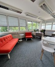 Aufenthaltsraum mit rotem Sofa und rotem Sessel. Daneben ein Regal mit Pflanzen und großer Fensterfront