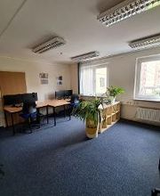 Arbeitsraum mit mehreren PC-Arbeitsplätzen, Regalen und Grünpflanzen.