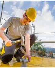 Montage-Elektiker Lehrling der mit Hammer und Helm ausgerüstet auf der Baustelle bei der Arbeit ist.