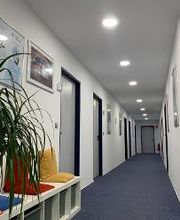 Flur mit kleiner Sitzbank und bunten Kissen. An der Wand hängen verschiedene Bilder im Rahmen. 