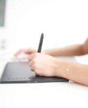 mediaService Bremen | Full-Stack Werbeagentur - Detailaufnahme einer Designerin bei der präzisen Arbeit mit einem Grafiktablett und digitalen Stift am Schreibtisch in einer modernen Designagentur.