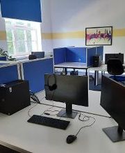 Arbeitsbereich mit 2 Computer-Bildschirmen, einer Tastatur, Maus und blauen Trennwänden. An der Wand im Hintergrund hängt ein buntes Bild.