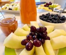 Gesundes Frühstück mit Teilnehmer:innen mit Melonen, Trauben, Tee und Saft.