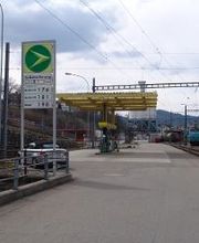 AGROLA Tankstelle in Herisau. Rechts Bahngleise gelegen. Tankstelle mit gelbem Gerüst. Im Vordergrund Totem mit AGROLA Diskus und Preisanzeigeschildern